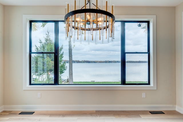 unfurnished dining area with hardwood / wood-style flooring, a notable chandelier, and a water view