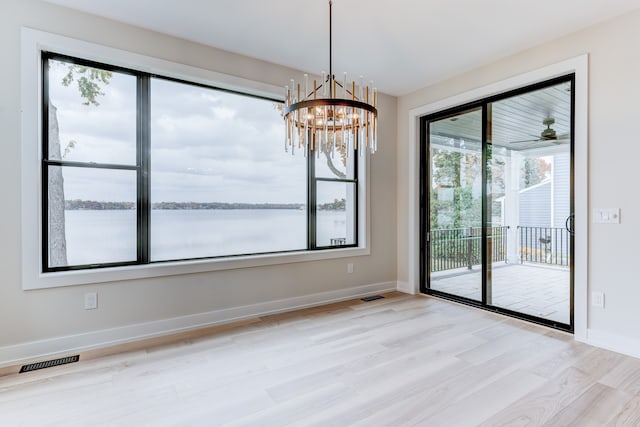 unfurnished dining area with a water view, light wood-type flooring, and an inviting chandelier