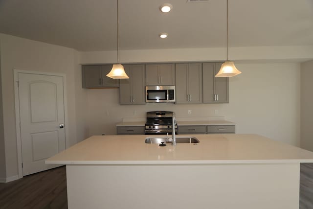 kitchen with dark wood-type flooring, gray cabinets, an island with sink, decorative light fixtures, and stainless steel appliances