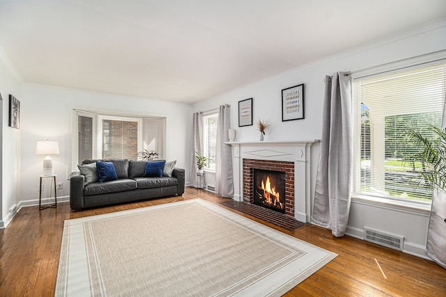 living room with hardwood / wood-style flooring, a healthy amount of sunlight, crown molding, and a brick fireplace