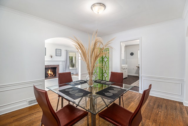 dining room with dark hardwood / wood-style flooring, ornamental molding, and a brick fireplace