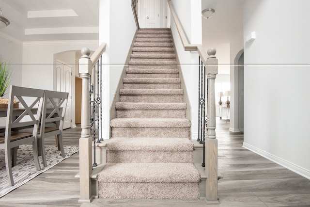 staircase with wood-type flooring and ornamental molding