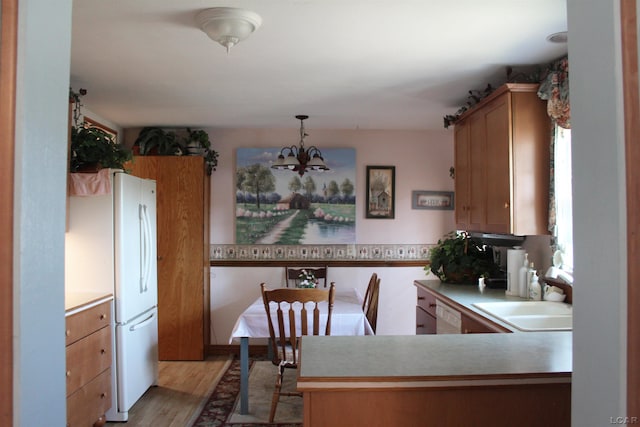 kitchen featuring kitchen peninsula, light wood-type flooring, white appliances, sink, and a notable chandelier