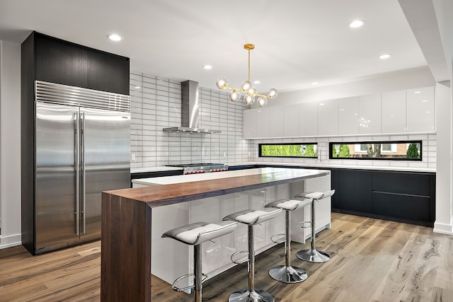 kitchen featuring hanging light fixtures, stainless steel appliances, wall chimney range hood, a kitchen island, and light wood-type flooring