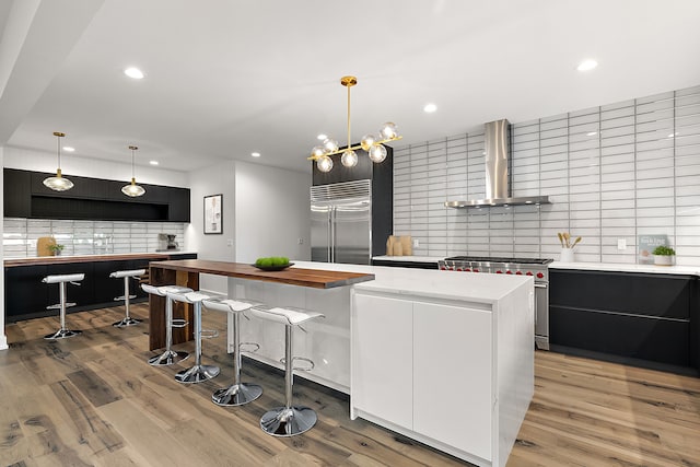 kitchen with premium appliances, dark cabinets, open shelves, a center island, and wall chimney exhaust hood