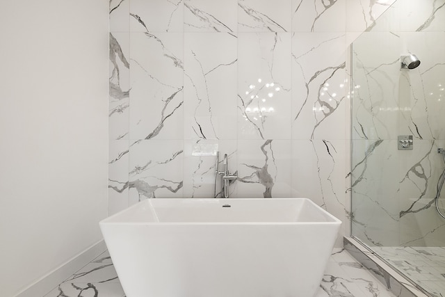 bathroom with marble finish floor, a freestanding bath, and stone wall