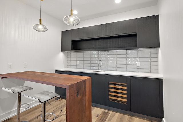 bar featuring hanging light fixtures, decorative backsplash, a sink, light wood-type flooring, and baseboards