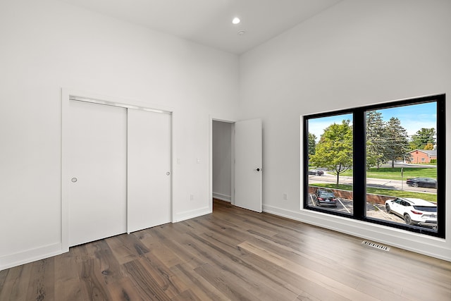 unfurnished bedroom with a closet, a towering ceiling, and hardwood / wood-style flooring