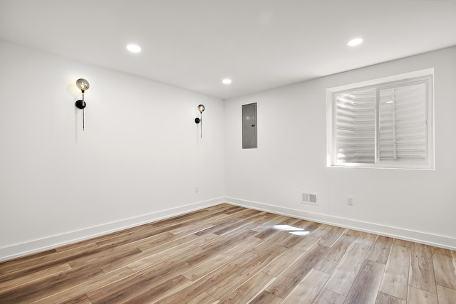 unfurnished room with electric panel, visible vents, light wood-style flooring, and baseboards