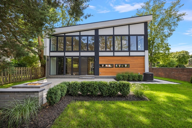 back of property with an outdoor fire pit, central AC, fence, a lawn, and a patio area