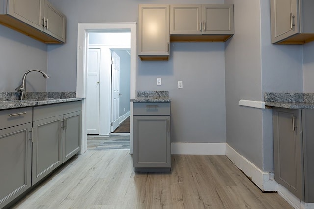 kitchen featuring gray cabinetry, light stone counters, sink, and light wood-type flooring