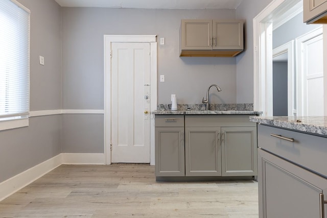 kitchen with light stone countertops, light hardwood / wood-style flooring, gray cabinetry, and sink