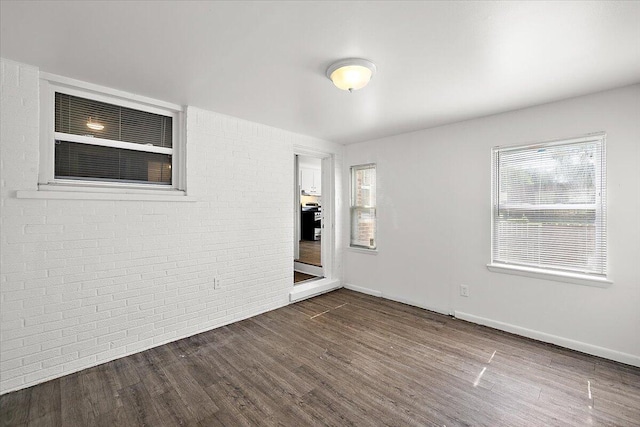 unfurnished room featuring brick wall and dark hardwood / wood-style floors