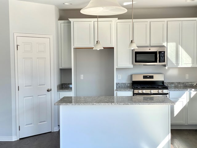 kitchen with white cabinets, appliances with stainless steel finishes, decorative light fixtures, and light stone countertops