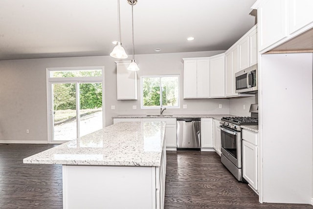 kitchen with white cabinetry, a center island, stainless steel appliances, light stone counters, and decorative light fixtures