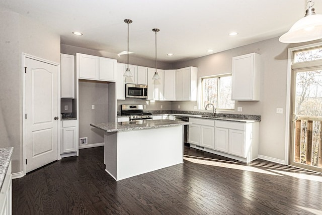 kitchen with light stone countertops, stainless steel appliances, decorative light fixtures, a center island, and white cabinetry