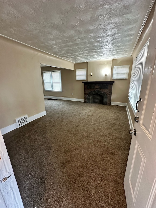 unfurnished living room featuring a textured ceiling, carpet floors, visible vents, baseboards, and a brick fireplace