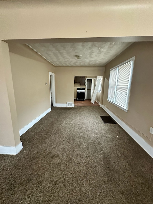 unfurnished living room with baseboards, visible vents, and dark carpet