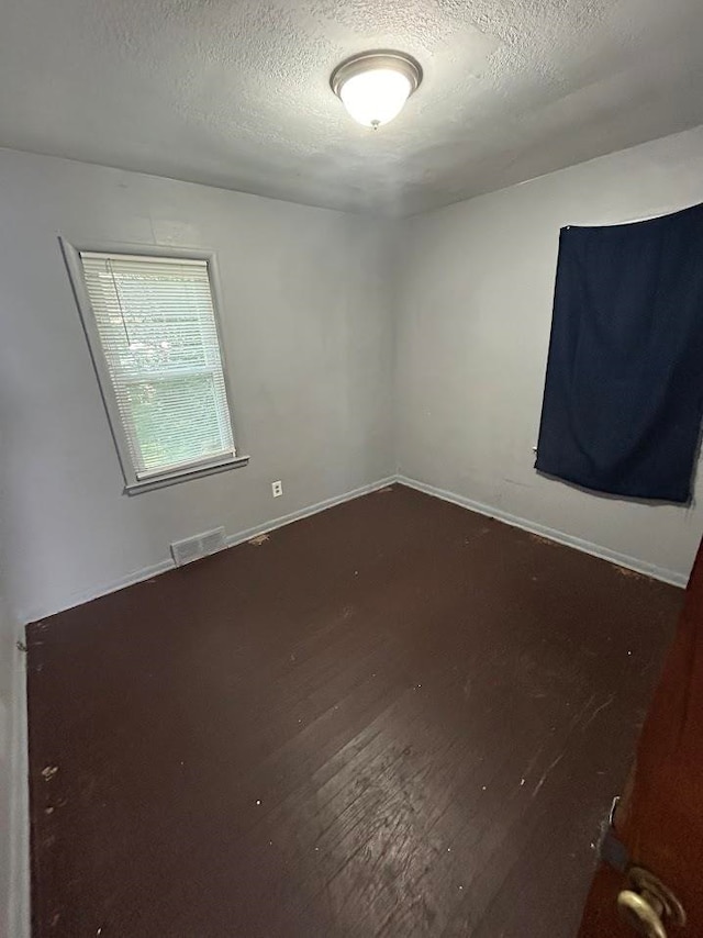 spare room featuring dark hardwood / wood-style flooring and a textured ceiling