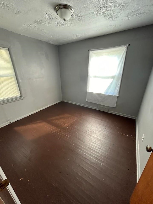 unfurnished room with a textured ceiling and dark wood-type flooring