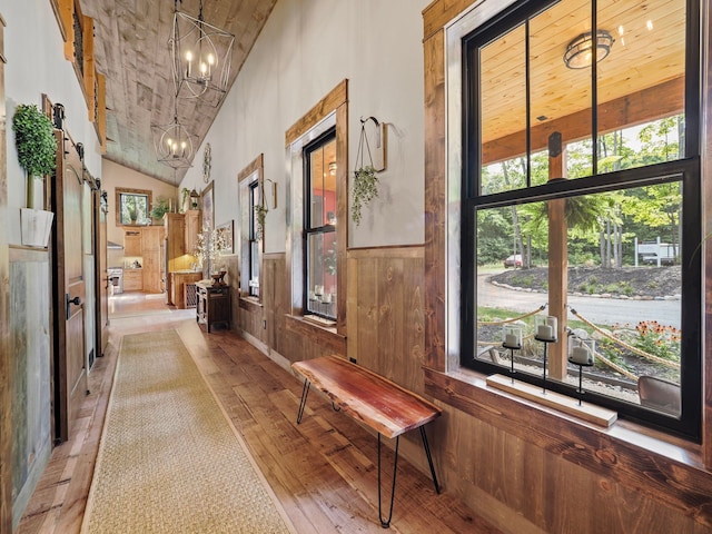 hall with wooden walls, lofted ceiling, a notable chandelier, a barn door, and light hardwood / wood-style flooring