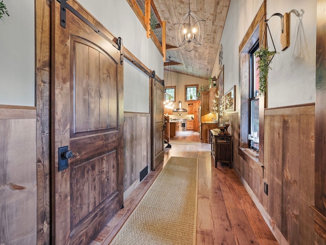 hall with lofted ceiling, a barn door, light hardwood / wood-style flooring, and wooden ceiling