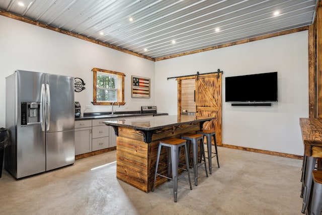 kitchen with a kitchen breakfast bar, stainless steel appliances, a barn door, white cabinetry, and a kitchen island