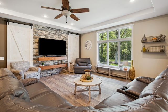 living room featuring a barn door, light hardwood / wood-style floors, ceiling fan, and a tray ceiling