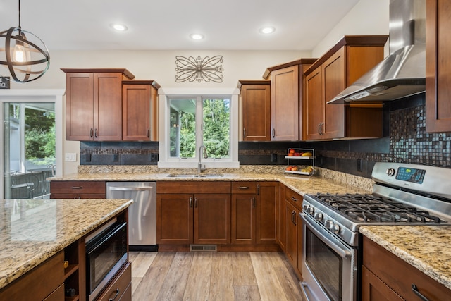 kitchen with stainless steel appliances, sink, wall chimney range hood, light hardwood / wood-style flooring, and hanging light fixtures