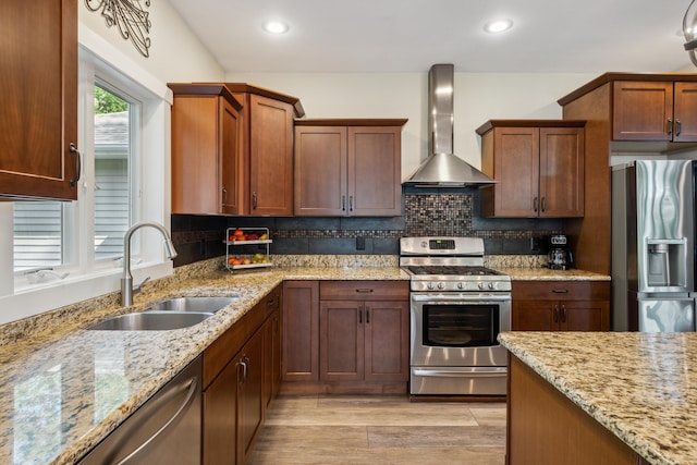 kitchen featuring light stone countertops, sink, wall chimney exhaust hood, stainless steel appliances, and light hardwood / wood-style flooring