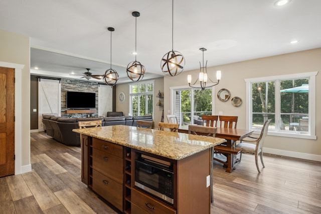 kitchen with decorative light fixtures, light hardwood / wood-style floors, stainless steel microwave, and ceiling fan with notable chandelier