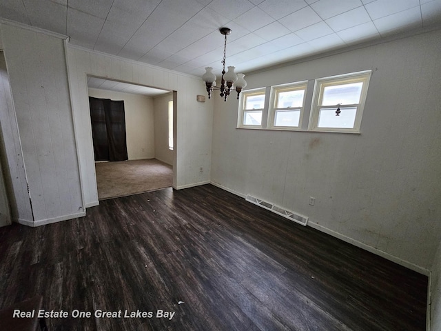 unfurnished dining area with dark hardwood / wood-style floors, crown molding, and an inviting chandelier