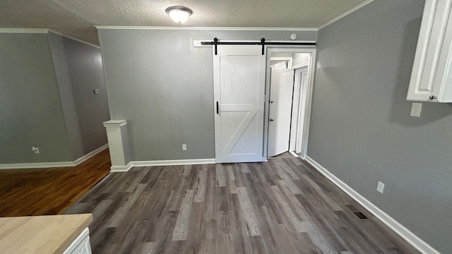 unfurnished bedroom featuring dark hardwood / wood-style floors, a barn door, ornamental molding, and a textured ceiling