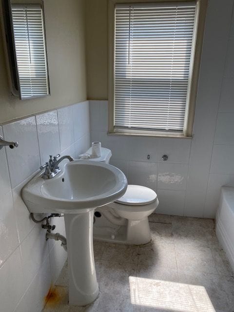 bathroom with a washtub, toilet, and tile walls