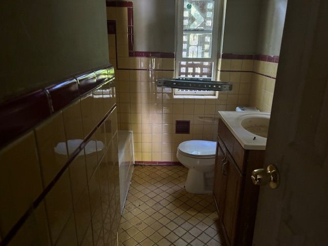 bathroom with tile patterned floors, vanity, toilet, and tile walls