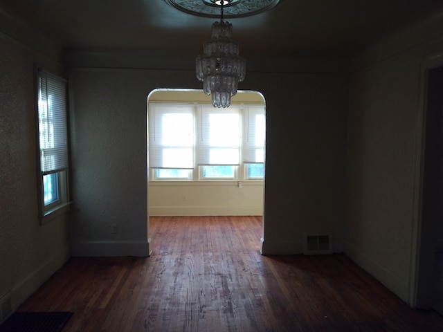 empty room with dark wood-type flooring and a chandelier