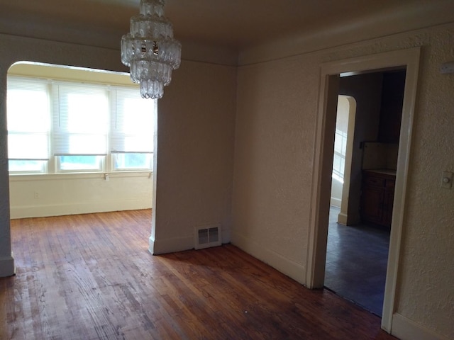 spare room with a notable chandelier and dark hardwood / wood-style flooring