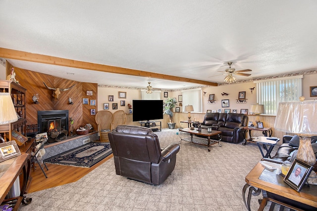 living room with wood walls, a wood stove, ceiling fan, light wood-type flooring, and a textured ceiling