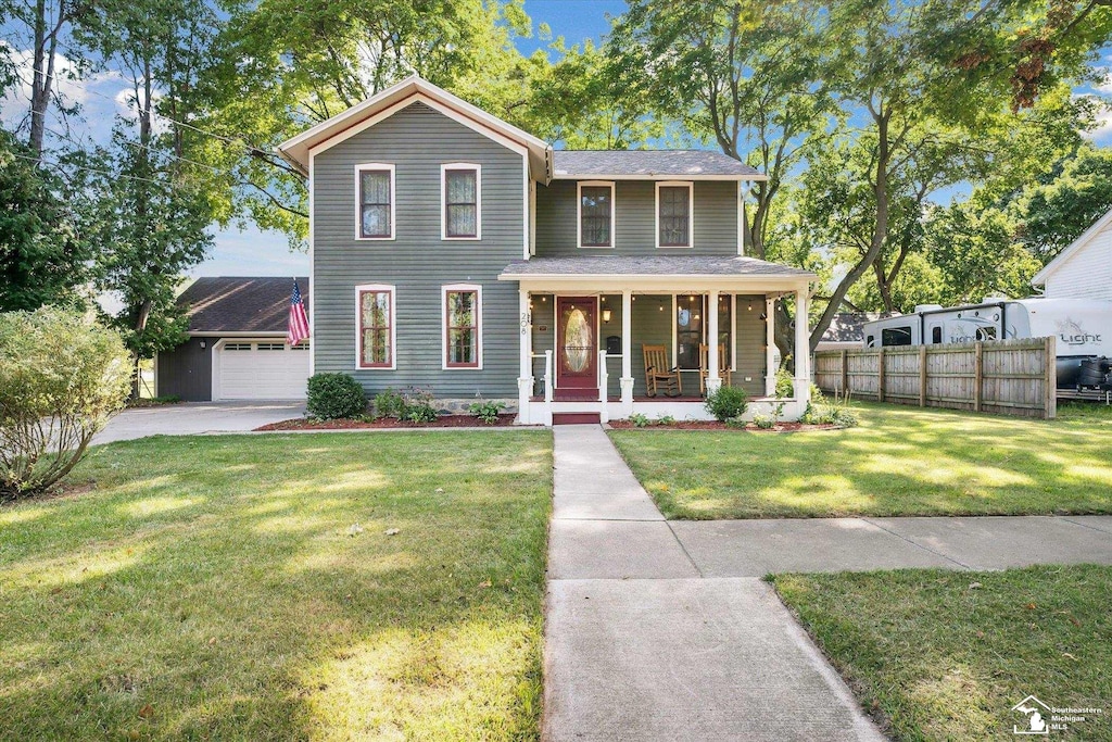 view of front facade featuring a front yard, a garage, covered porch, and an outbuilding