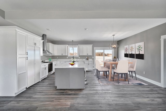 kitchen featuring a kitchen island, appliances with stainless steel finishes, white cabinets, hanging light fixtures, and wall chimney exhaust hood