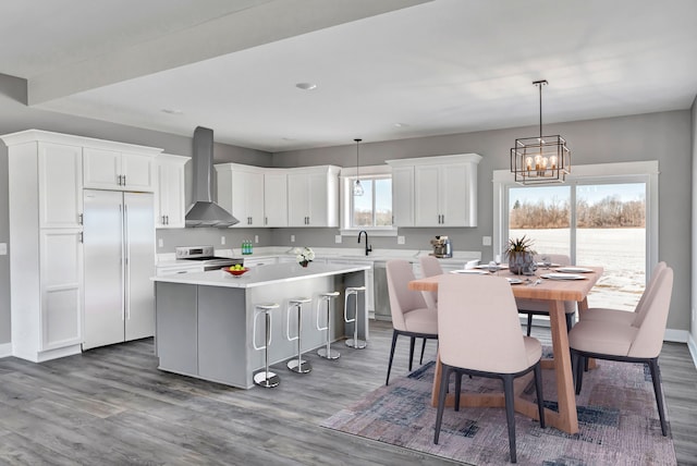 kitchen featuring a kitchen island, wall chimney range hood, white cabinets, and decorative light fixtures