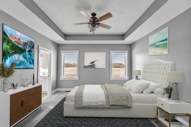 bedroom featuring multiple windows, light hardwood / wood-style flooring, ceiling fan, and a tray ceiling