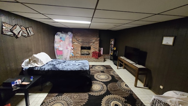 tiled bedroom featuring a fireplace, wood walls, and a drop ceiling