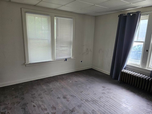 spare room with a paneled ceiling, radiator heating unit, and dark wood-type flooring