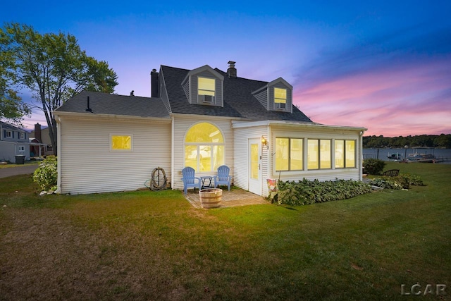 back house at dusk featuring a lawn and a patio area