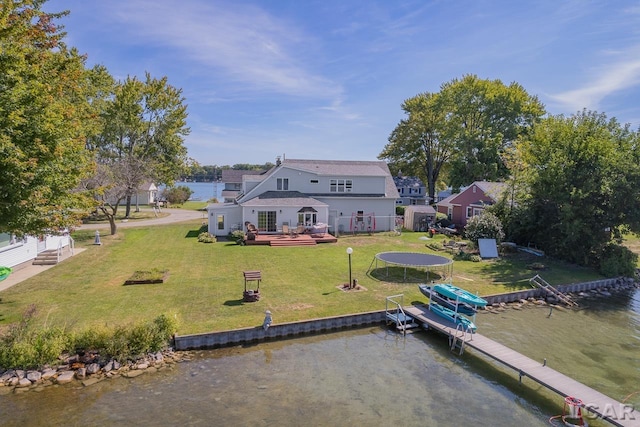 back of house featuring a deck with water view, a trampoline, and a lawn