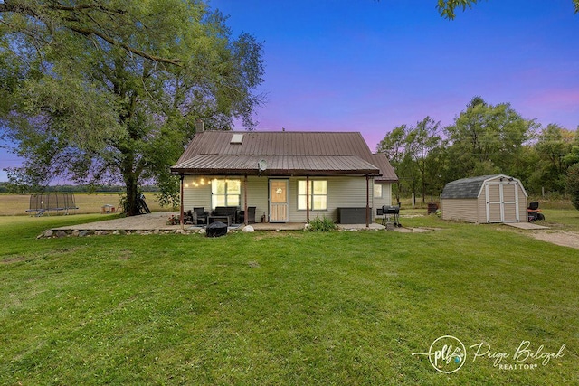 back house at dusk with a lawn, a storage shed, a patio, and a trampoline