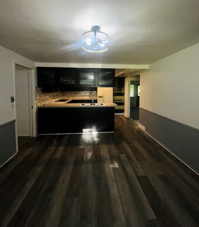 kitchen with decorative backsplash, dark hardwood / wood-style flooring, kitchen peninsula, and sink