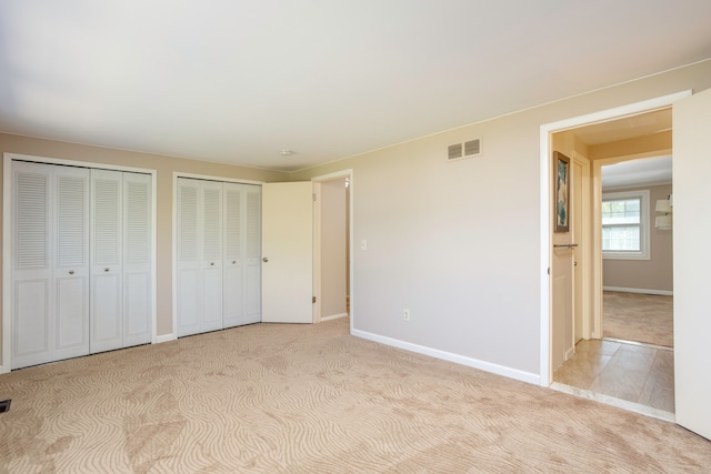 unfurnished bedroom with light colored carpet and multiple closets