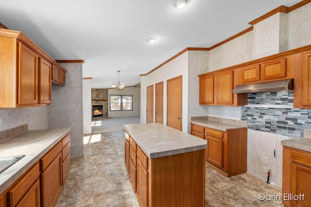 kitchen featuring extractor fan, a kitchen island, a large fireplace, decorative backsplash, and crown molding